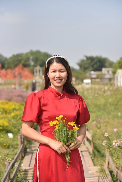 Young Woman in a Dress Standing Outside and Holding Flowers