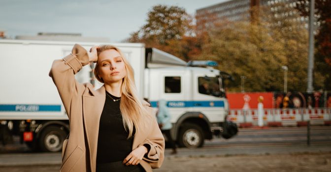 Stylish woman in coat posing on a city street with a truck in the background.