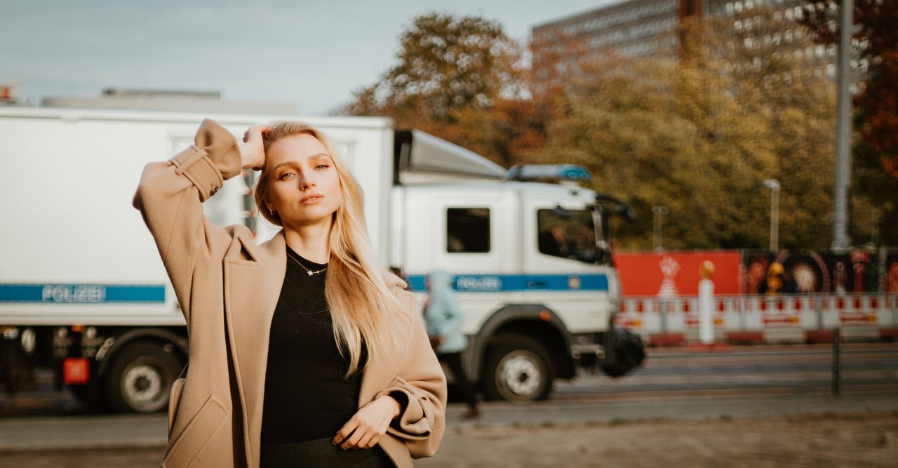 stylish woman in coat posing on a city street with a truck in the back