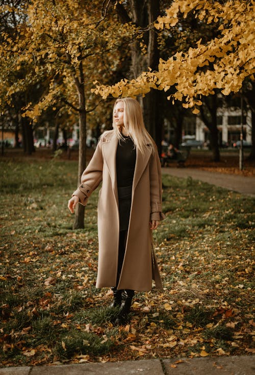 Young Woman in Coat Standing on the Background of Autumnal Trees in a Park 