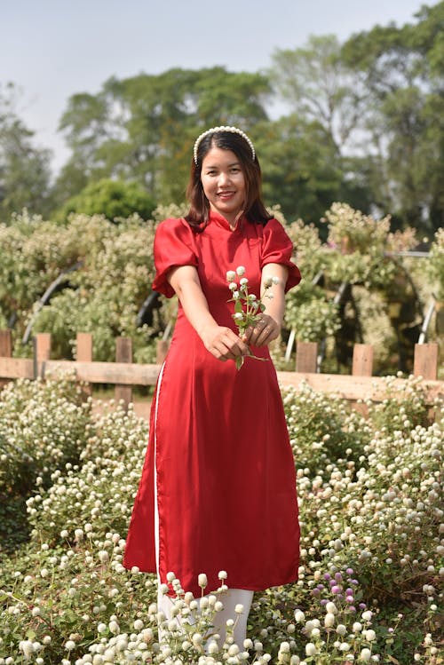 Young Woman in a Dress Standing on a Meadow and Holding Flowers