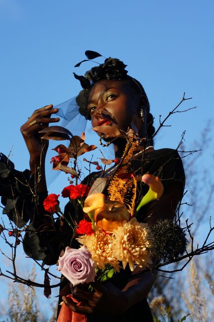 Fashion portrait of a model holding a bouquet of colorful flowers with a clear blue sky backdrop.