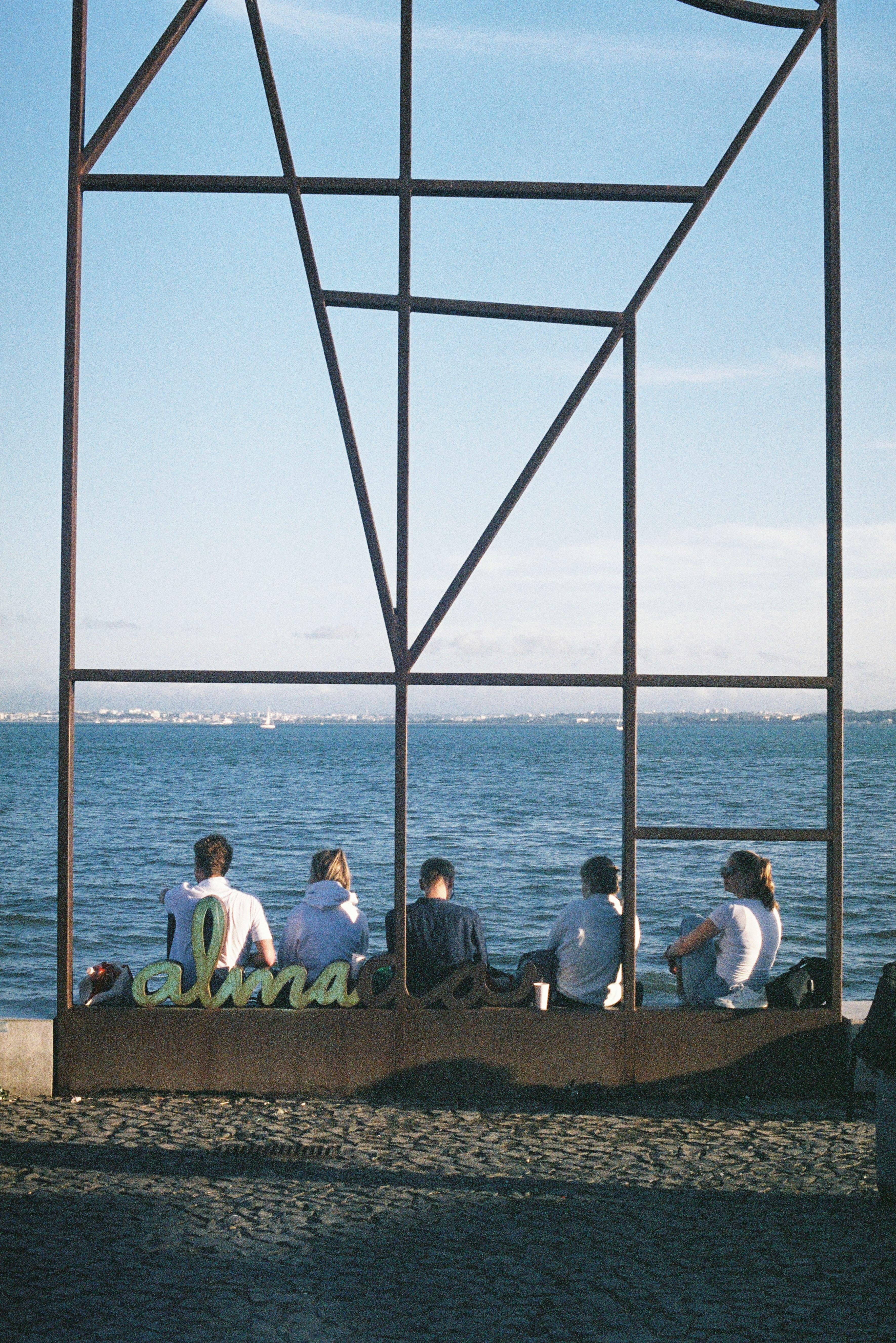 A scenic view of people sitting along the Lisbon promenade by the sea, enjoying the daylight.