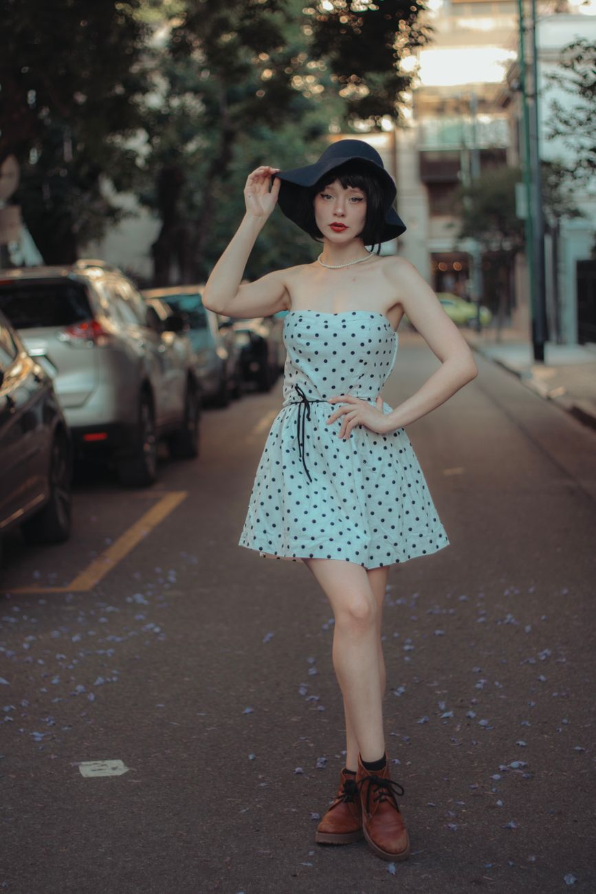 Elegant young woman in a polka dot dress and hat posing on a city street in Buenos Aires, Argentina.