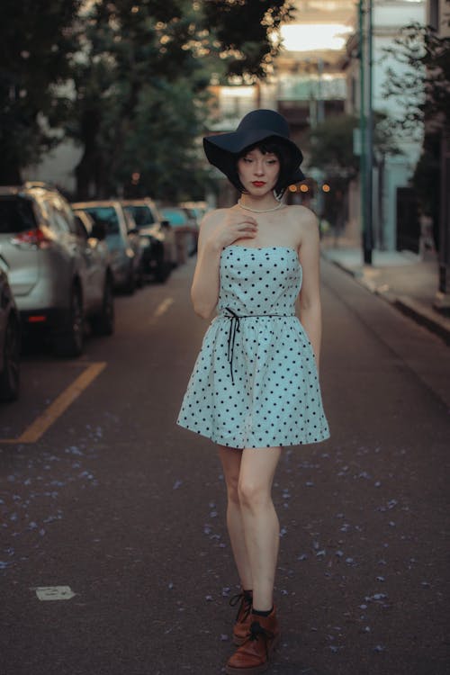 Young Woman in a Polka Dot Dress and Hat Standing on the Street 