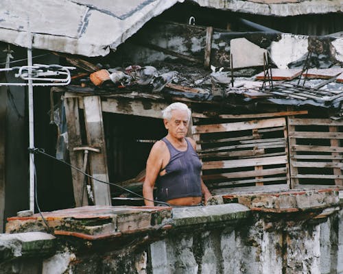 Elderly Man Standing beside a Broken Abandoned Building 