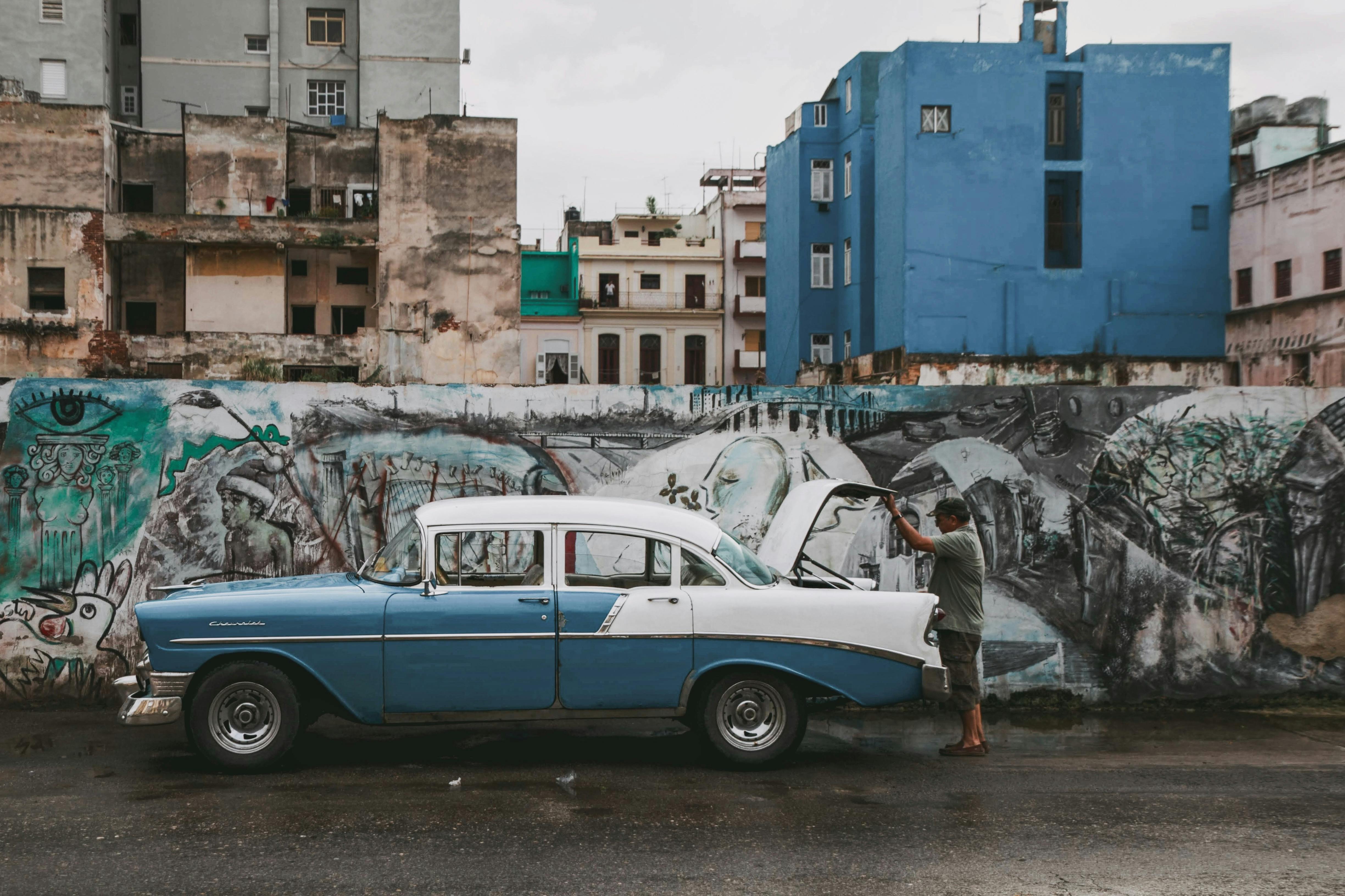 Classic vintage car parked on a Havana street against a graffiti-covered wall.