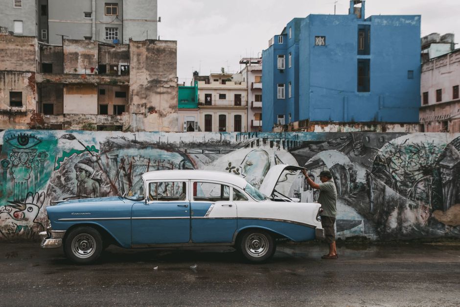 Classic vintage car parked on a Havana street against a graffiti-covered wall.