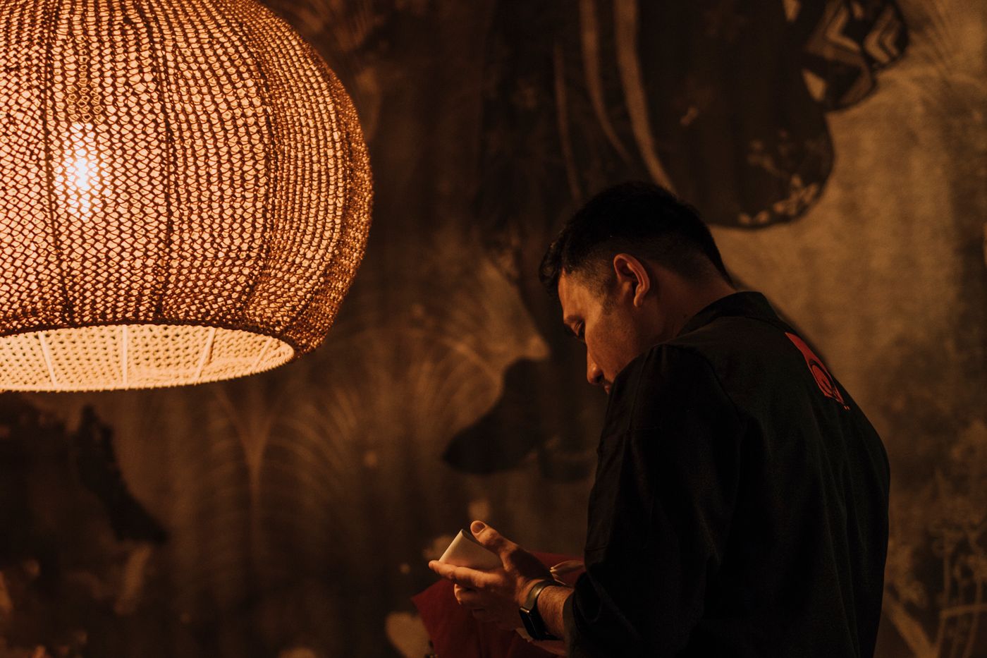 A waiter in a dimly lit restaurant leaning attentively over a table, captured under warm pendant lighting
