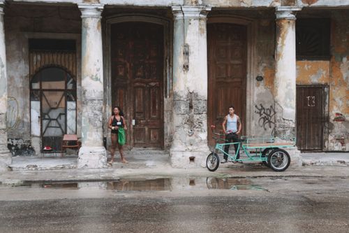 Free A weathered street scene with two people, columns, and a rickshaw on a wet day. Stock Photo