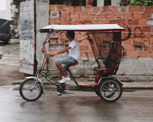 Free A man rides a rickshaw through a rainy street in a gritty urban environment. Stock Photo