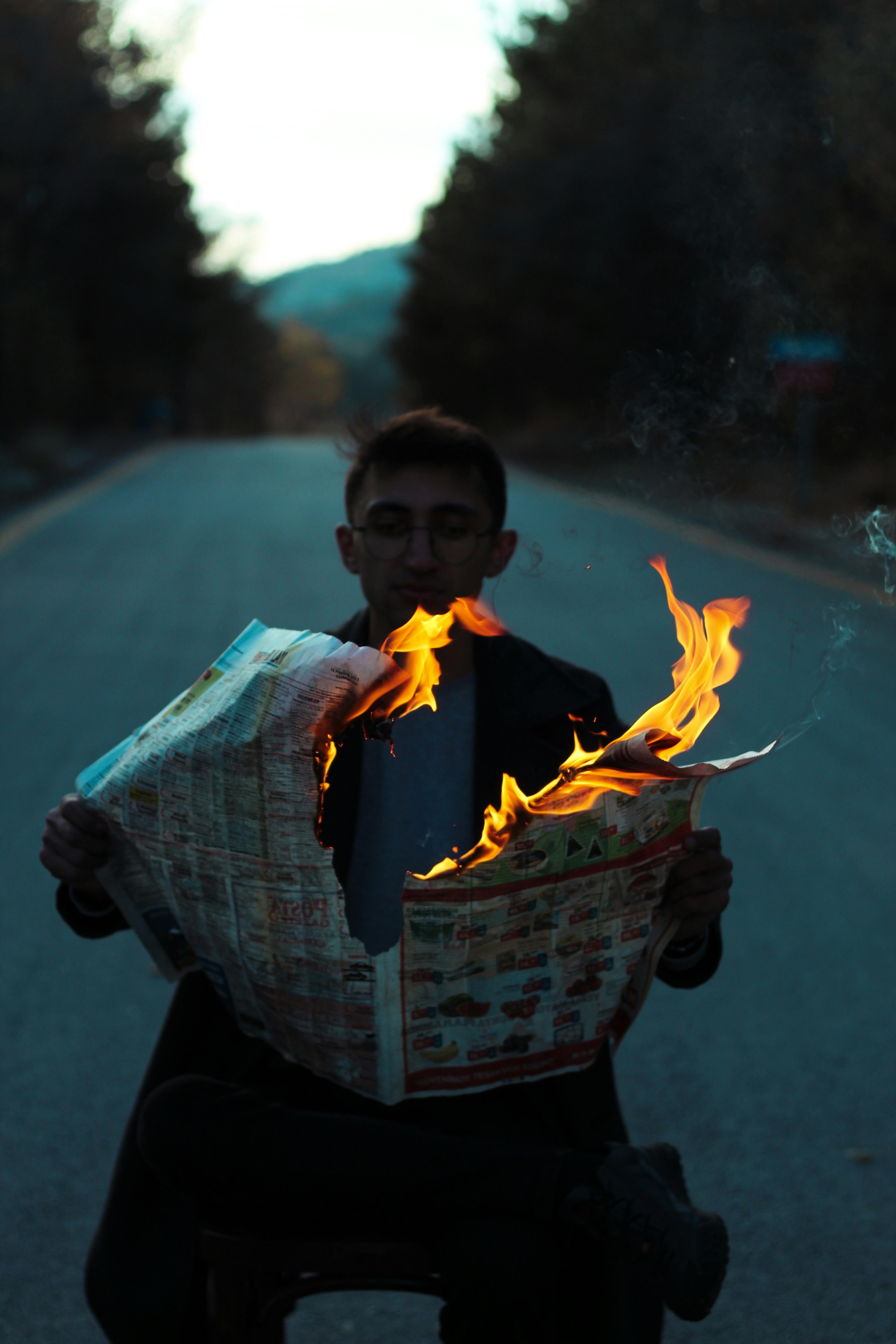 man sitting in the middle of a road and holding a burning newspaper