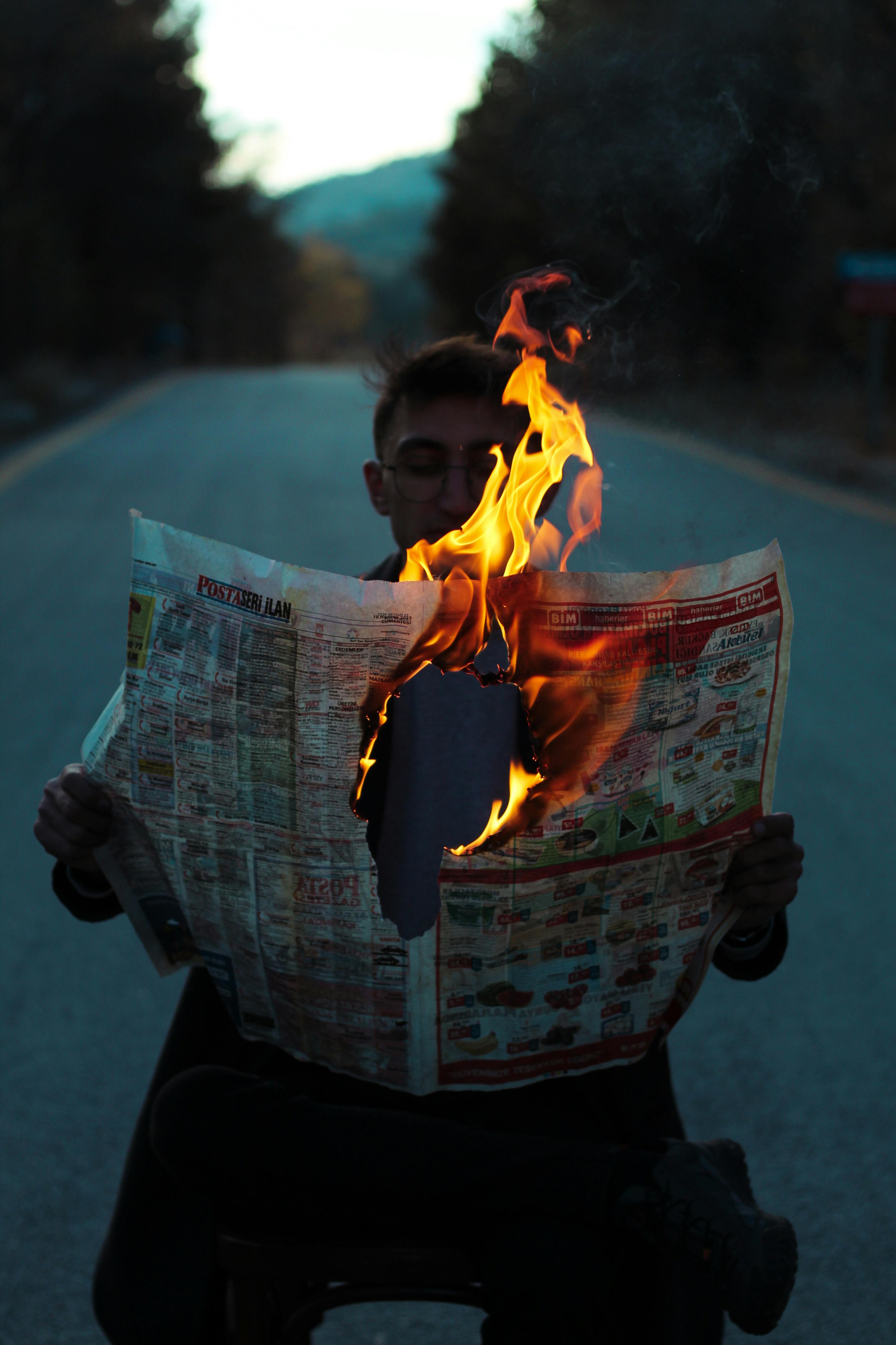 man sitting in the middle of a road and holding a burning newspaper