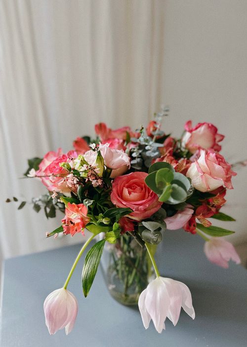 Free Mixed bouquet of roses and tulips in a glass vase on a table, perfect for home decor. Stock Photo