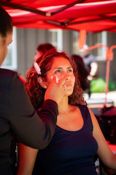 A woman enjoys professional makeup under a red canopy, creating a vibrant outdoor beauty scene.