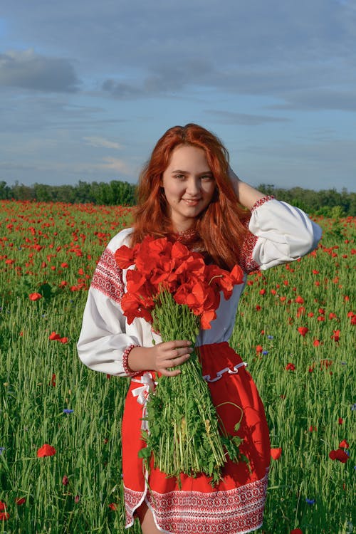 Young Redhead Standing on a Field with a Bouquet of Poppies 