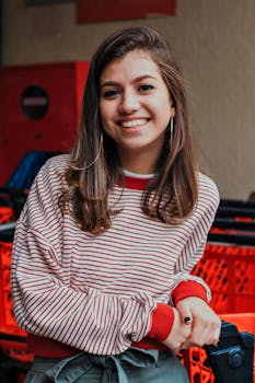 一位穿着条纹毛衣的开朗女人在红色购物车上摆着姿势，散发出快乐的氛围