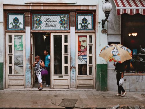 Free A vibrant vintage bookshop facade with people under umbrellas on a city street. Stock Photo