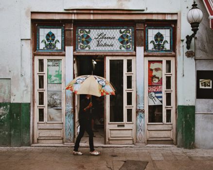 A person walks with a colorful umbrella by a historic bookstore with stained glass decor.