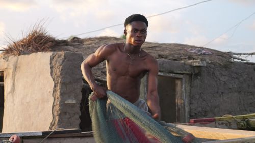 Free Shirtless young man fishing with a net in a rustic village setting, showcasing strength and skill. Stock Photo