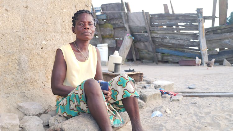 Senior Woman Sitting On A Ground In A Village