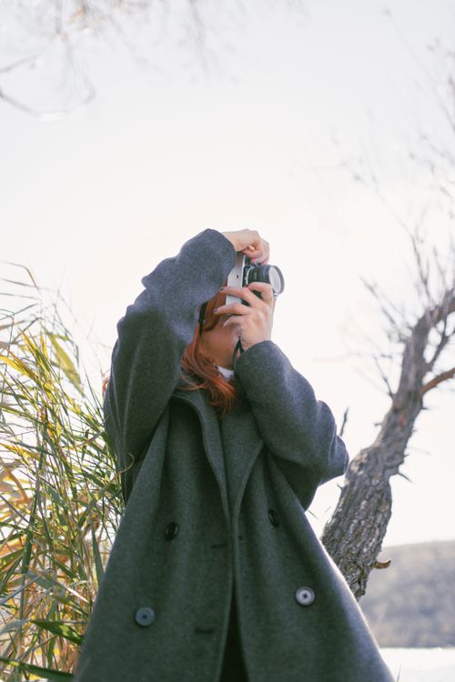 Free A woman in a coat captures the beauty of autumn with her camera outdoors. Stock Photo