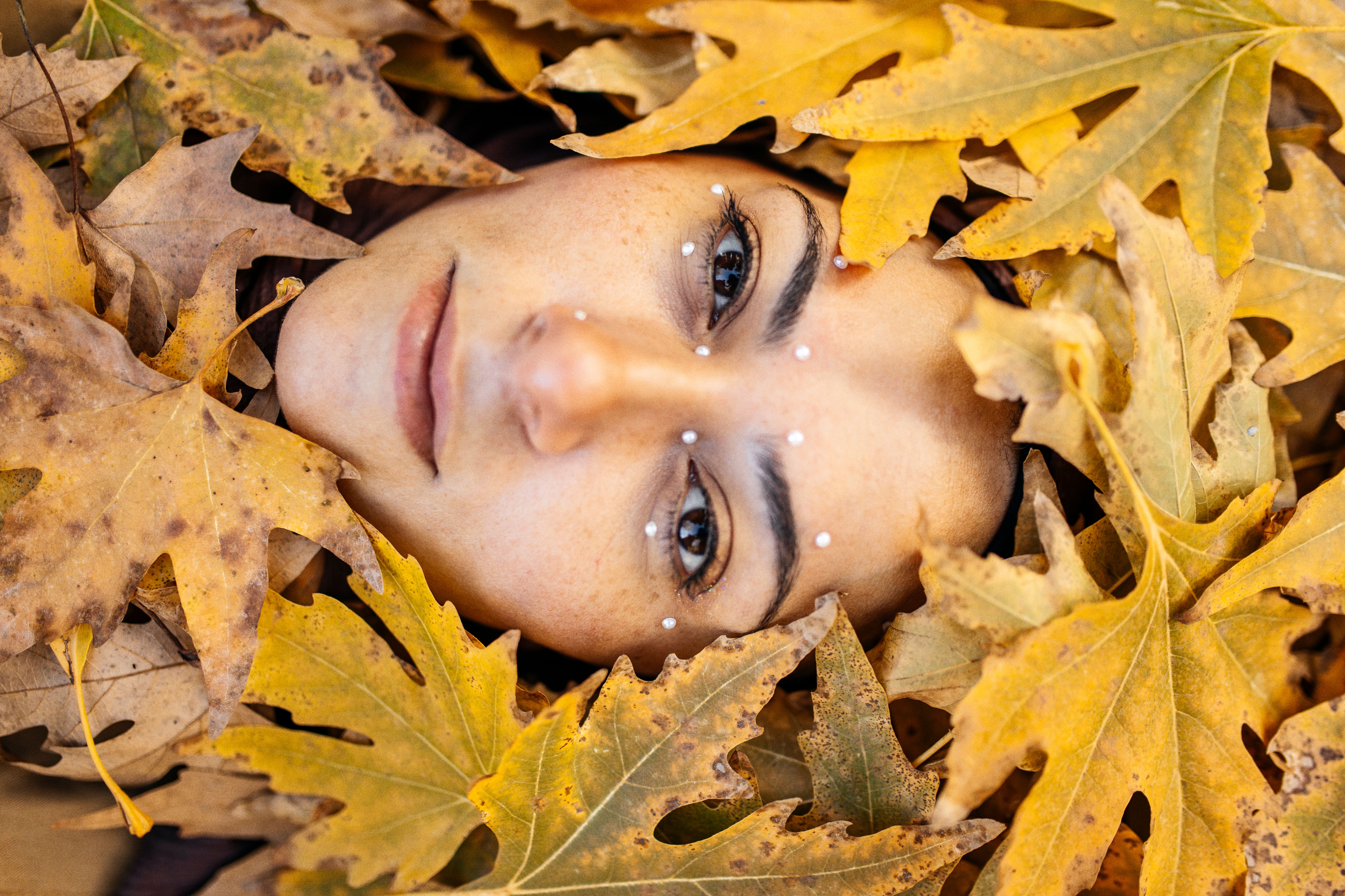 A woman laying in a pile of leaves with her eyes closed · Free Stock Photo