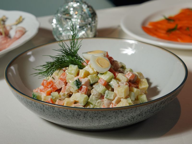 Colorful vegetable salad garnished with dill and quail eggs in a speckled ceramic bowl.