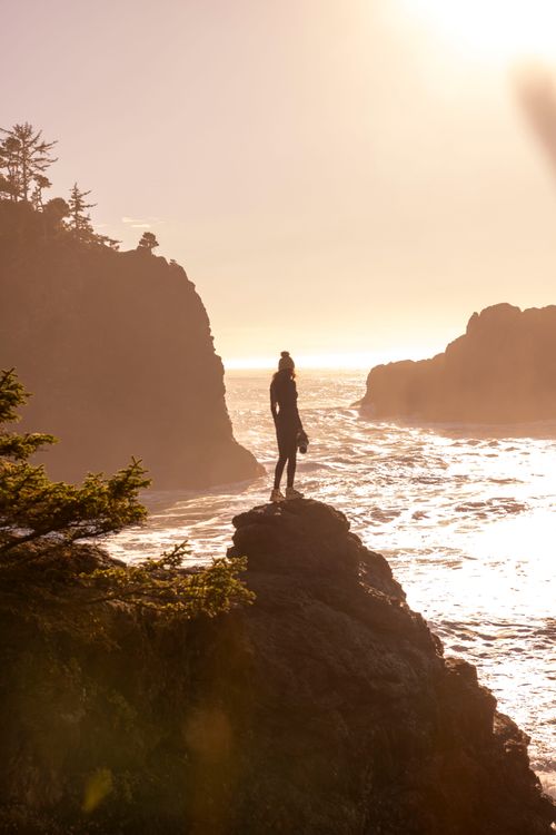 Free Silhouette of a woman standing on cliffs by the ocean at sunrise, exuding serenity and freedom. Stock Photo
