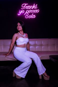 Fashionable woman posing with neon pink sign in stylish nightlife setting.