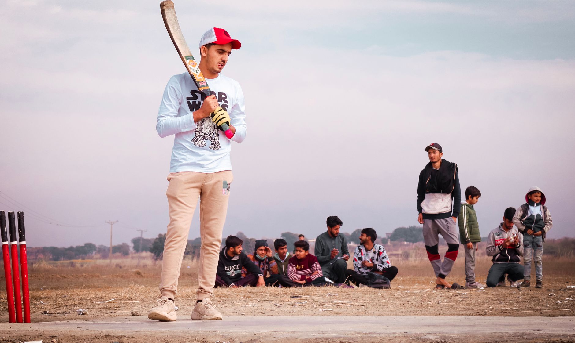 A group of young males engaged in a cricket match outdoors on a sunny day.