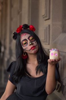 Woman with sugar skull makeup holding a decorative skull for Day of the Dead celebration.