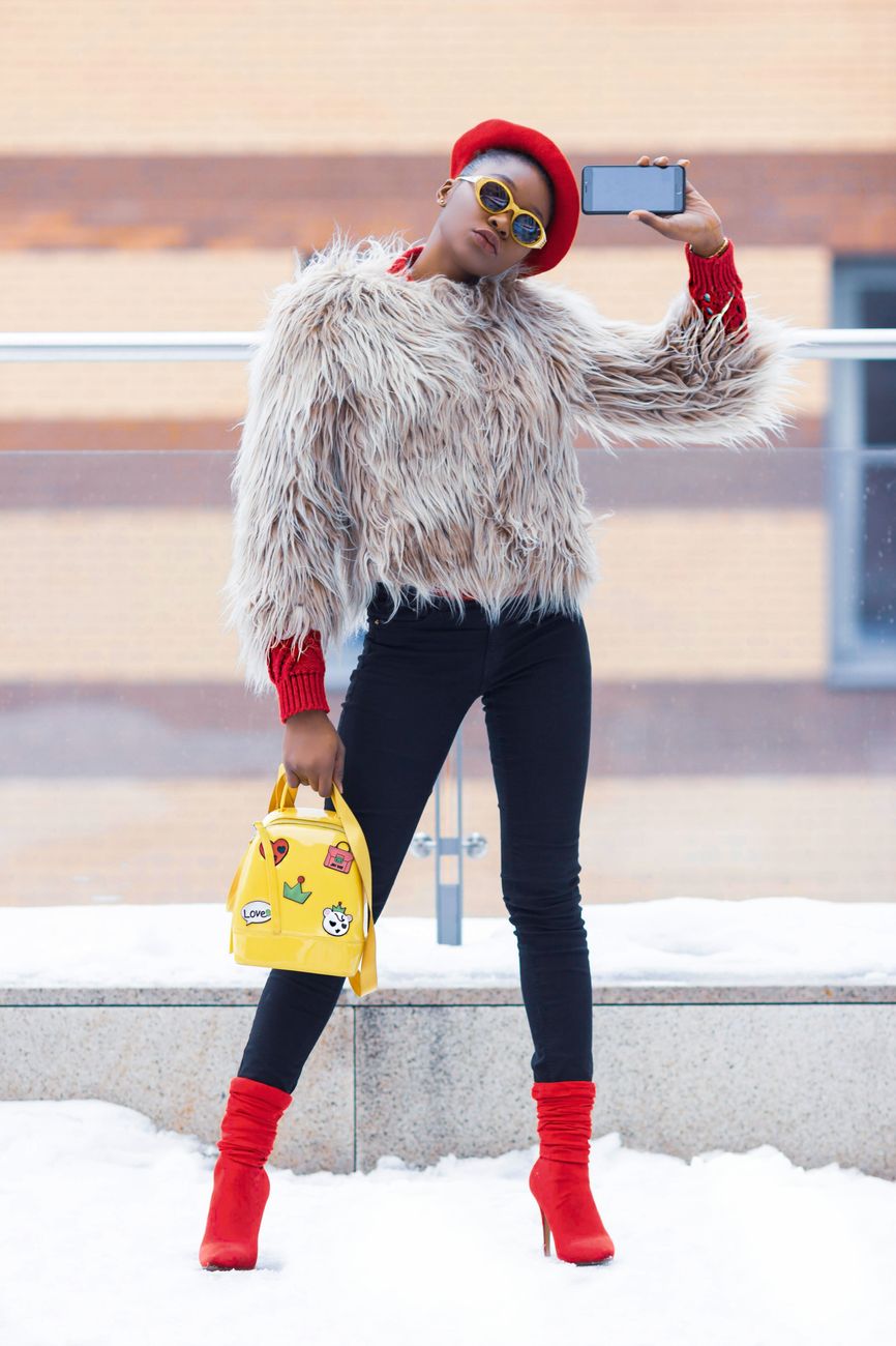 Chic woman in trendy winter attire poses for a selfie in snowy surroundings.