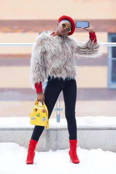 Chic woman in trendy winter attire poses for a selfie in snowy surroundings.