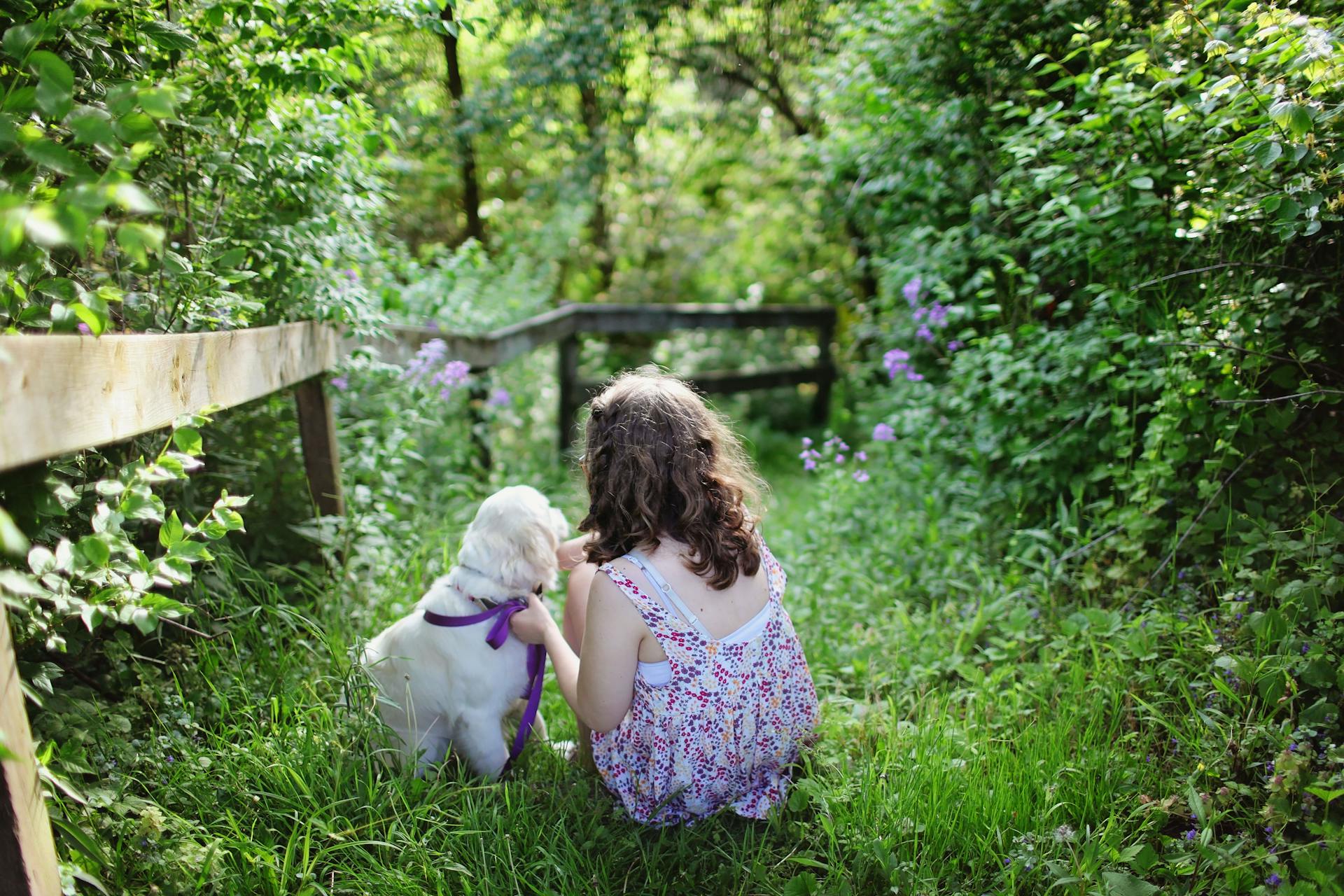 Une fille et un chiot assis sur de l'herbe verte entourés de plantes pendant la journée