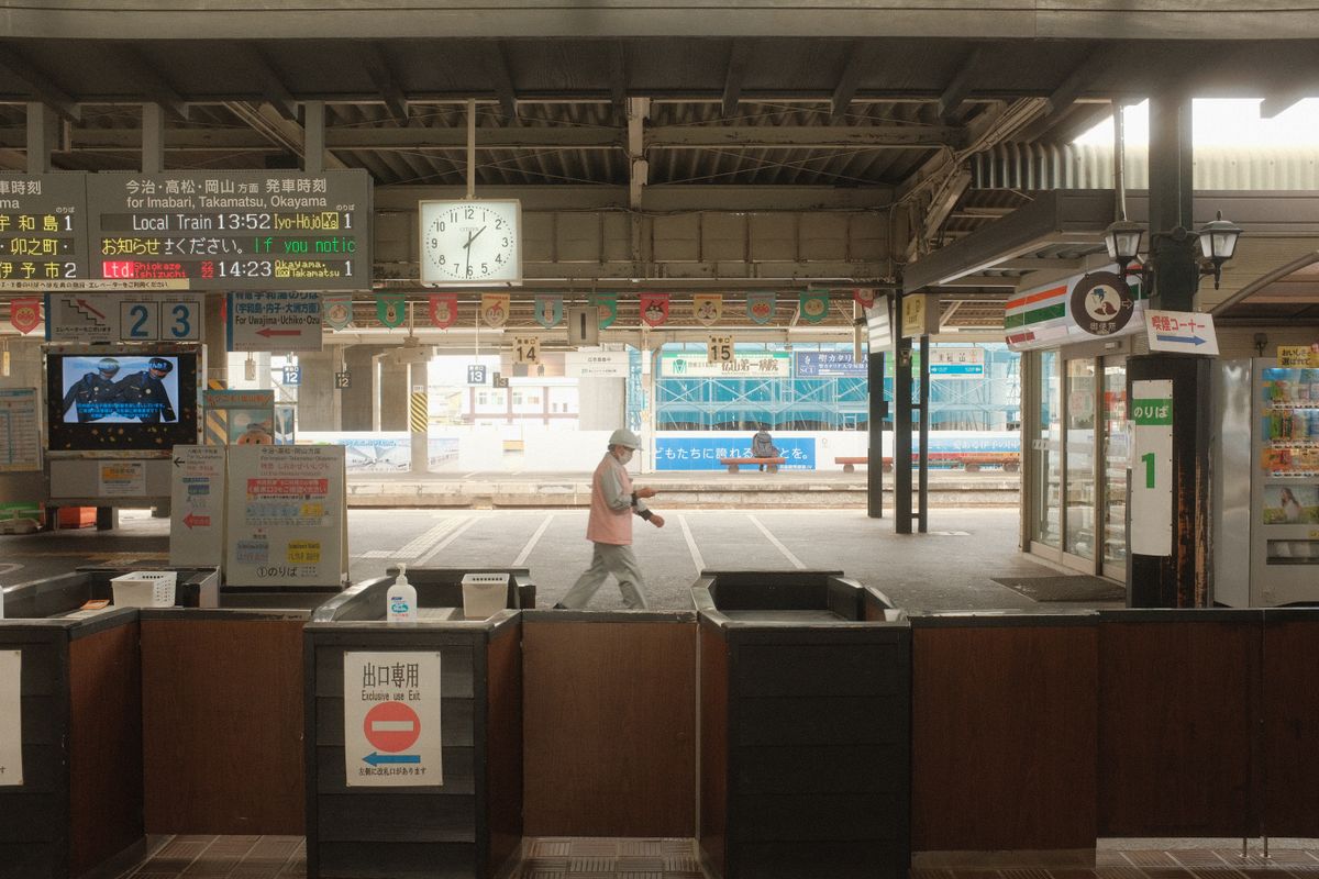 Person walking through a bustling Japanese train station featuring signs, vending machines, and a clock