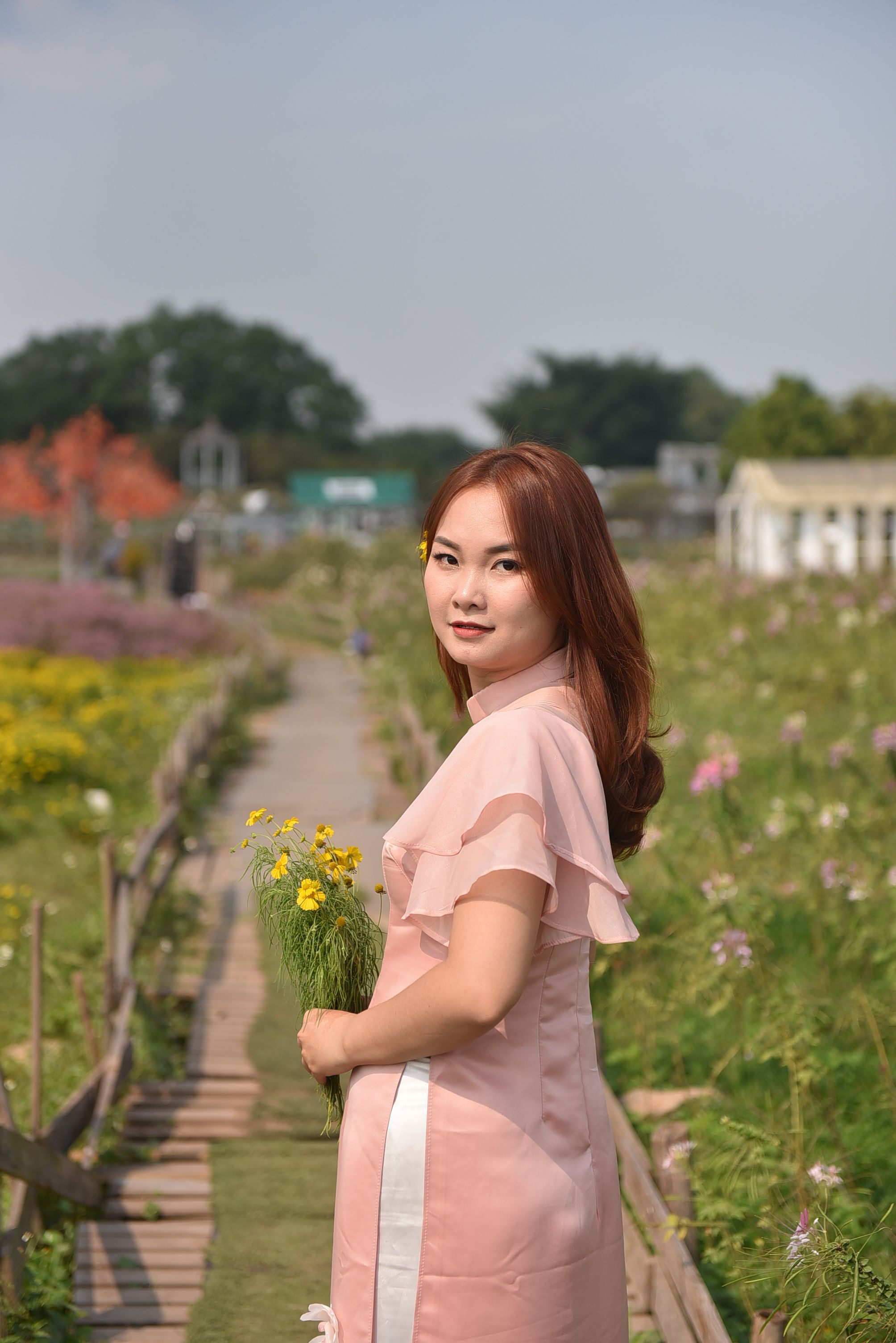 Photo of a Woman Wearing a Pink Dress Holding Yellow Flowers in a ...