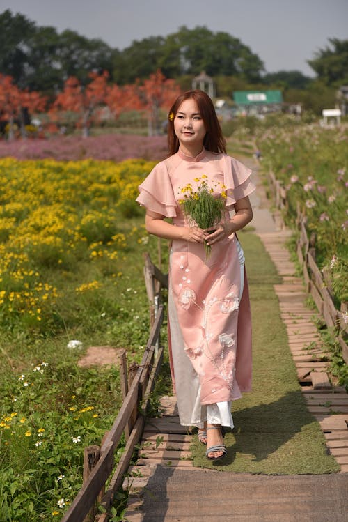Photo of a Woman Wearing an Elegant Dress, Holding a Bouquet in a Garden