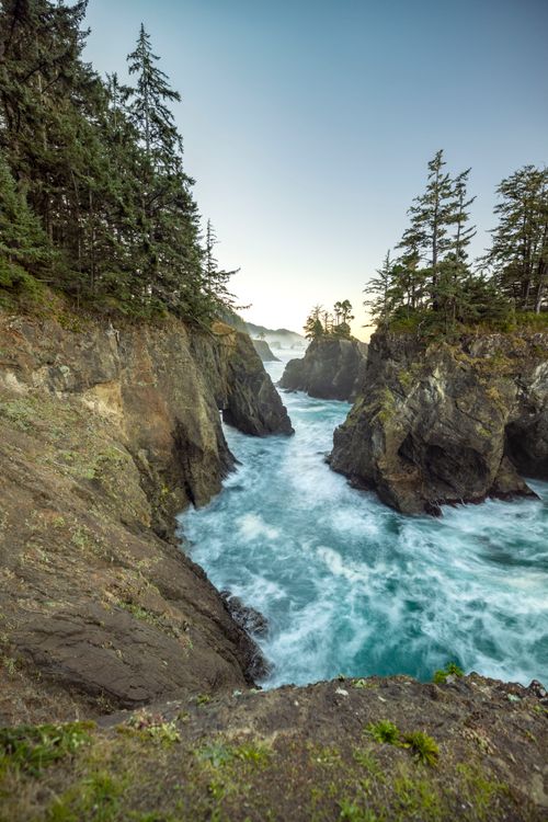 Free Breathtaking view of rugged coastal cliffs and a powerful flowing river, surrounded by lush forests. Stock Photo