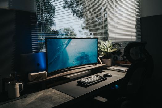 Stylish home office setup with a curved monitor and indoor plant, illuminated by natural light.