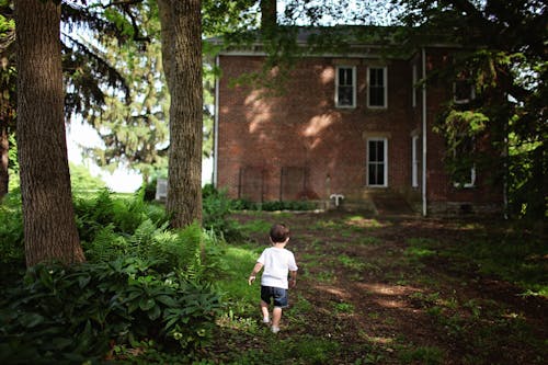 Boy Wearing White Crew Neck T Shirt and Blue Denim Shorts Walking Towards Brown Concrete Building