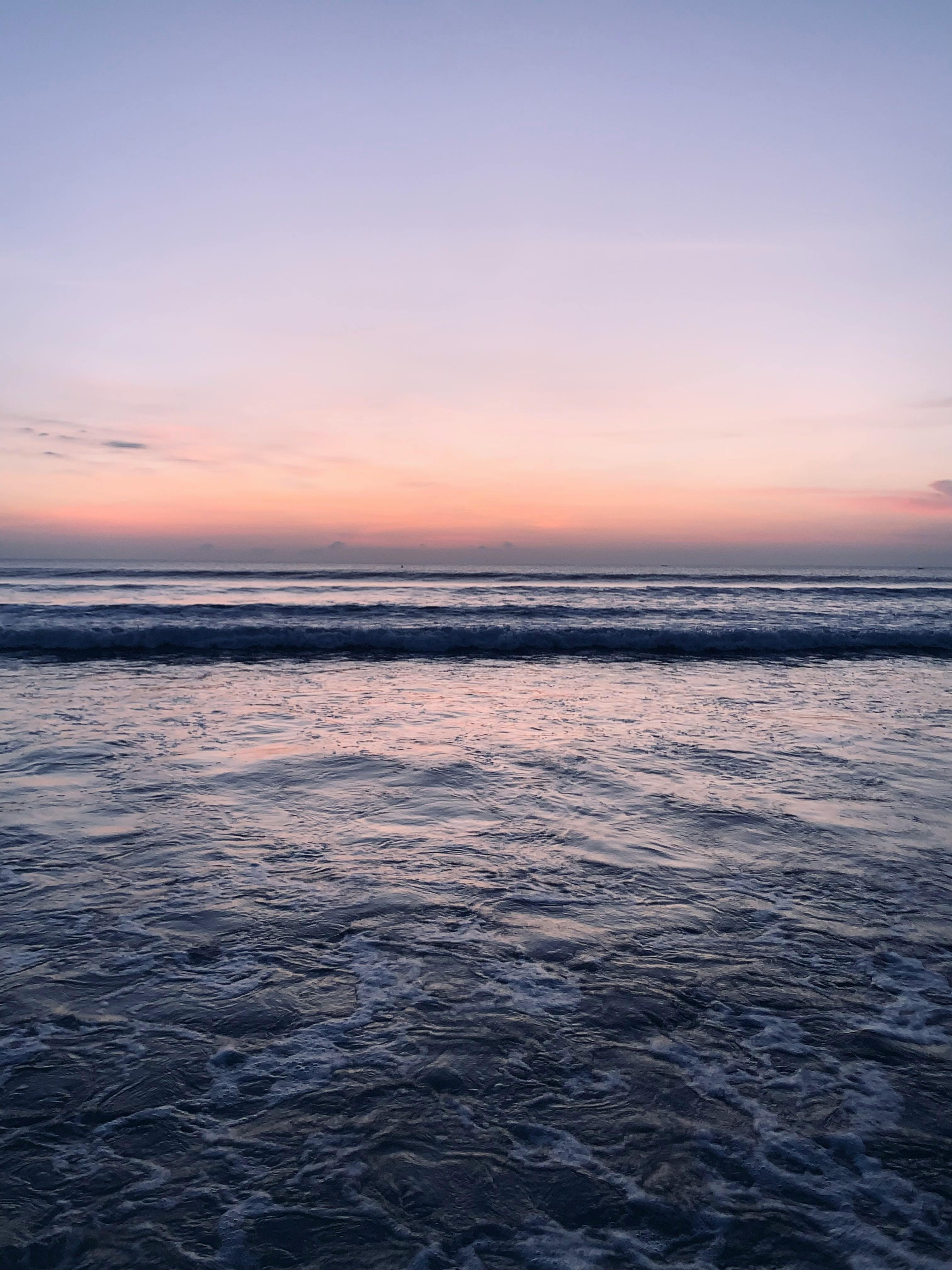 A serene view of ocean waves under a pink and purple sunset sky, perfect for relaxation themes.