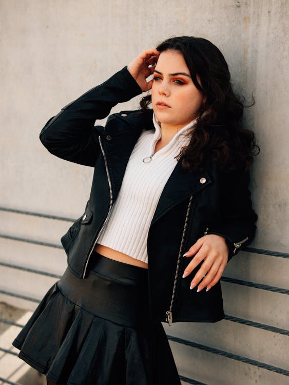 A woman in a leather skirt leaning against a wall