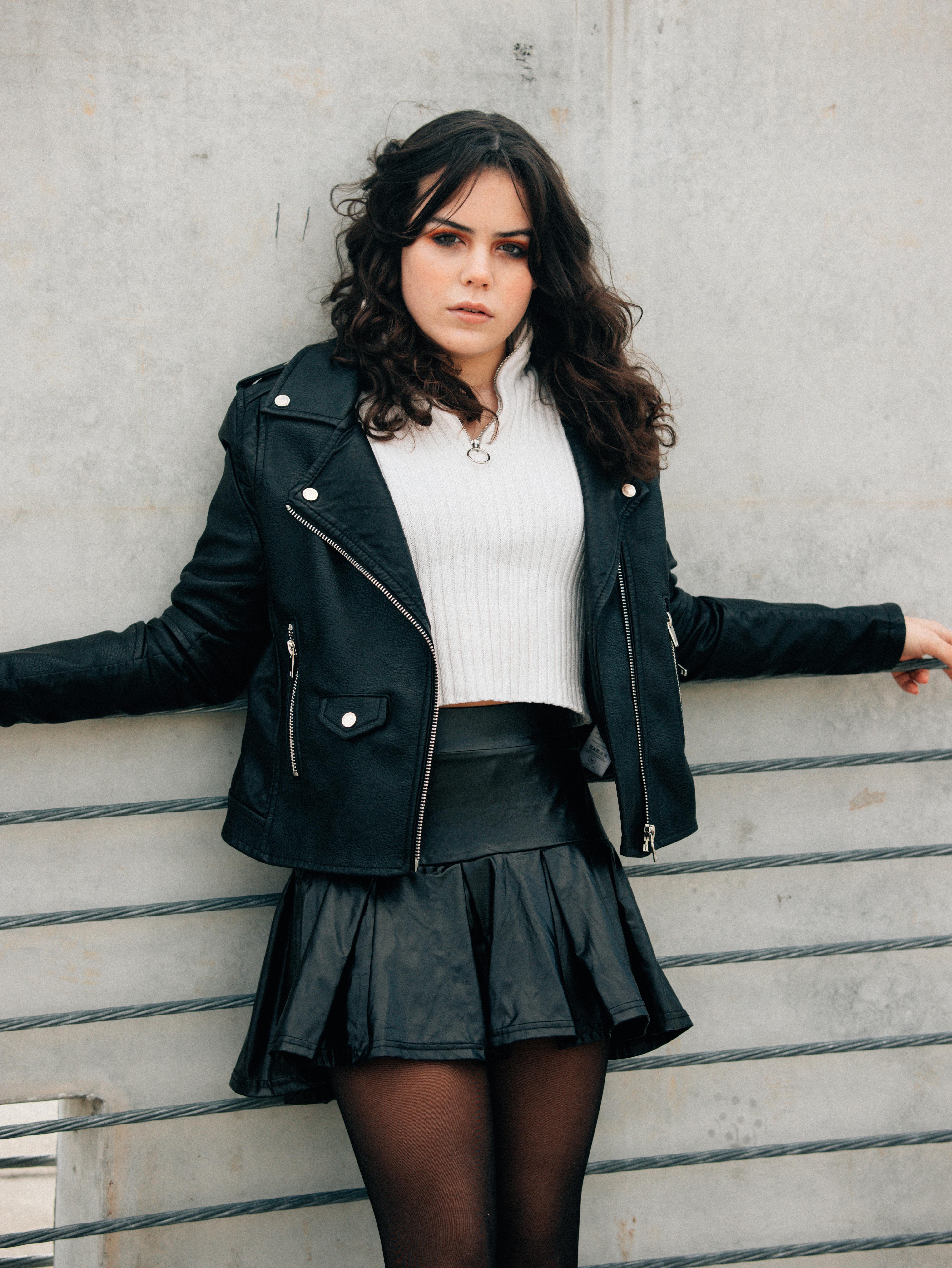 a woman in a leather skirt leaning against a wall