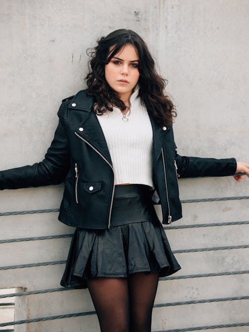 A woman in a leather skirt leaning against a wall