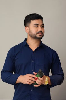 Portrait of an adult man in a navy blue shirt, holding a smartphone, exuding confidence and style.