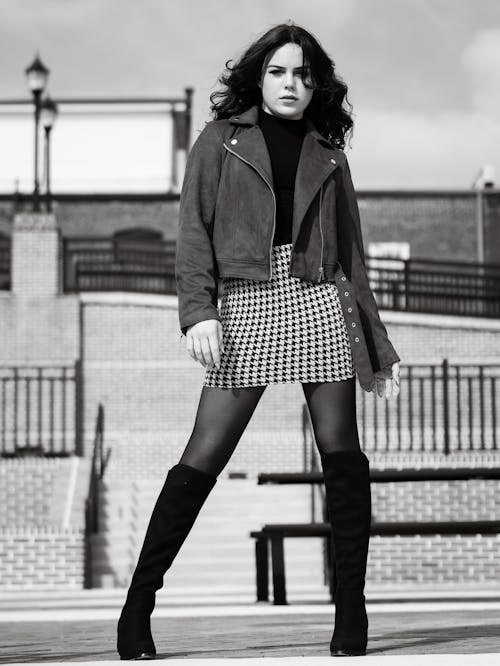 A woman in a skirt and jacket posing on a sidewalk