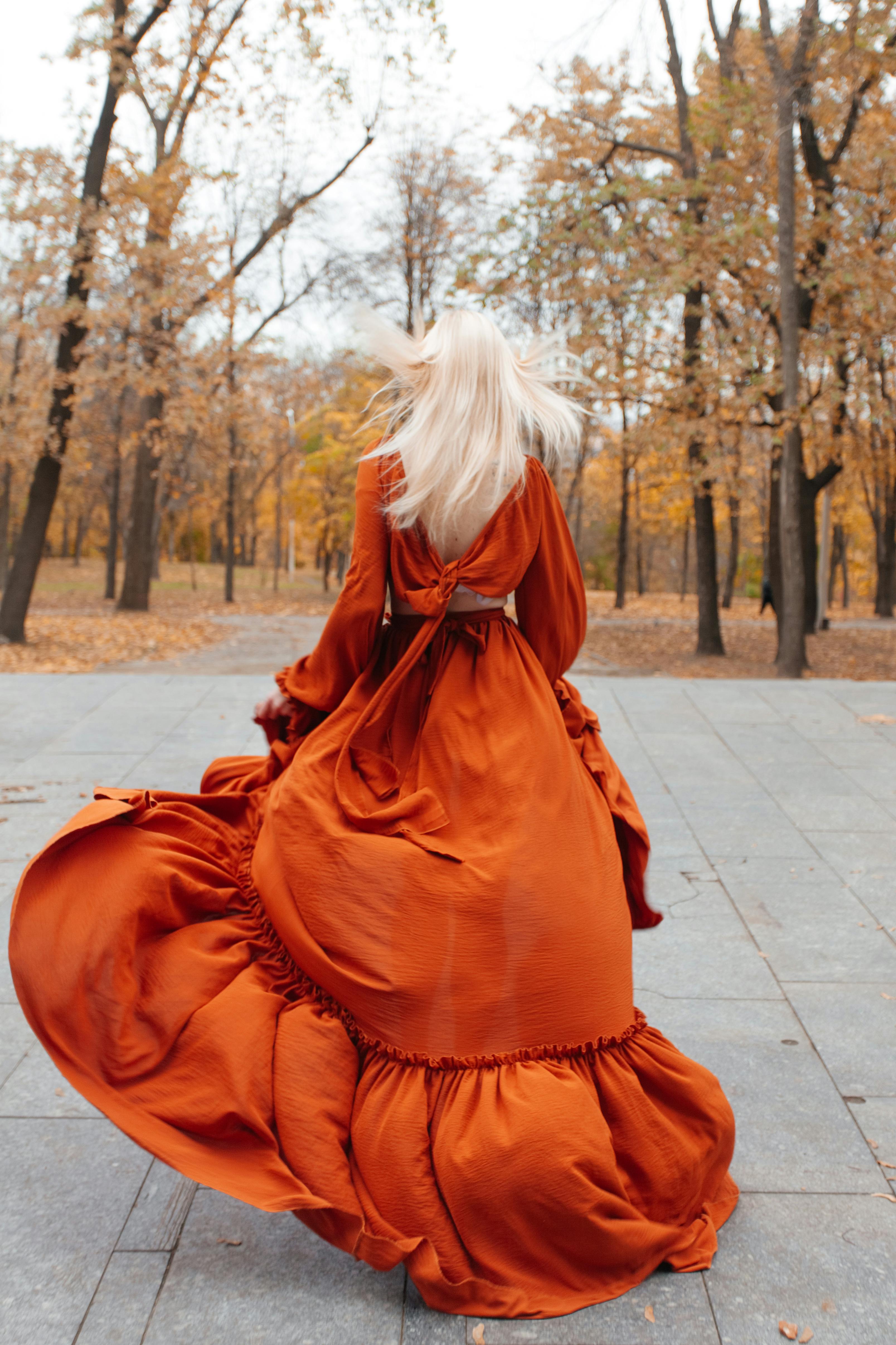 A woman in an orange dress is walking through a park  Free Stock Photo