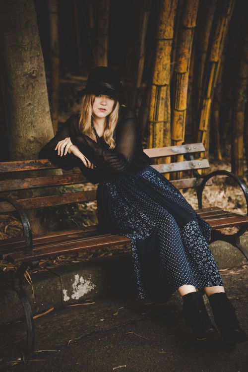 Free A fashionable woman elegantly posing on a park bench wearing a stylish dress and hat. Stock Photo