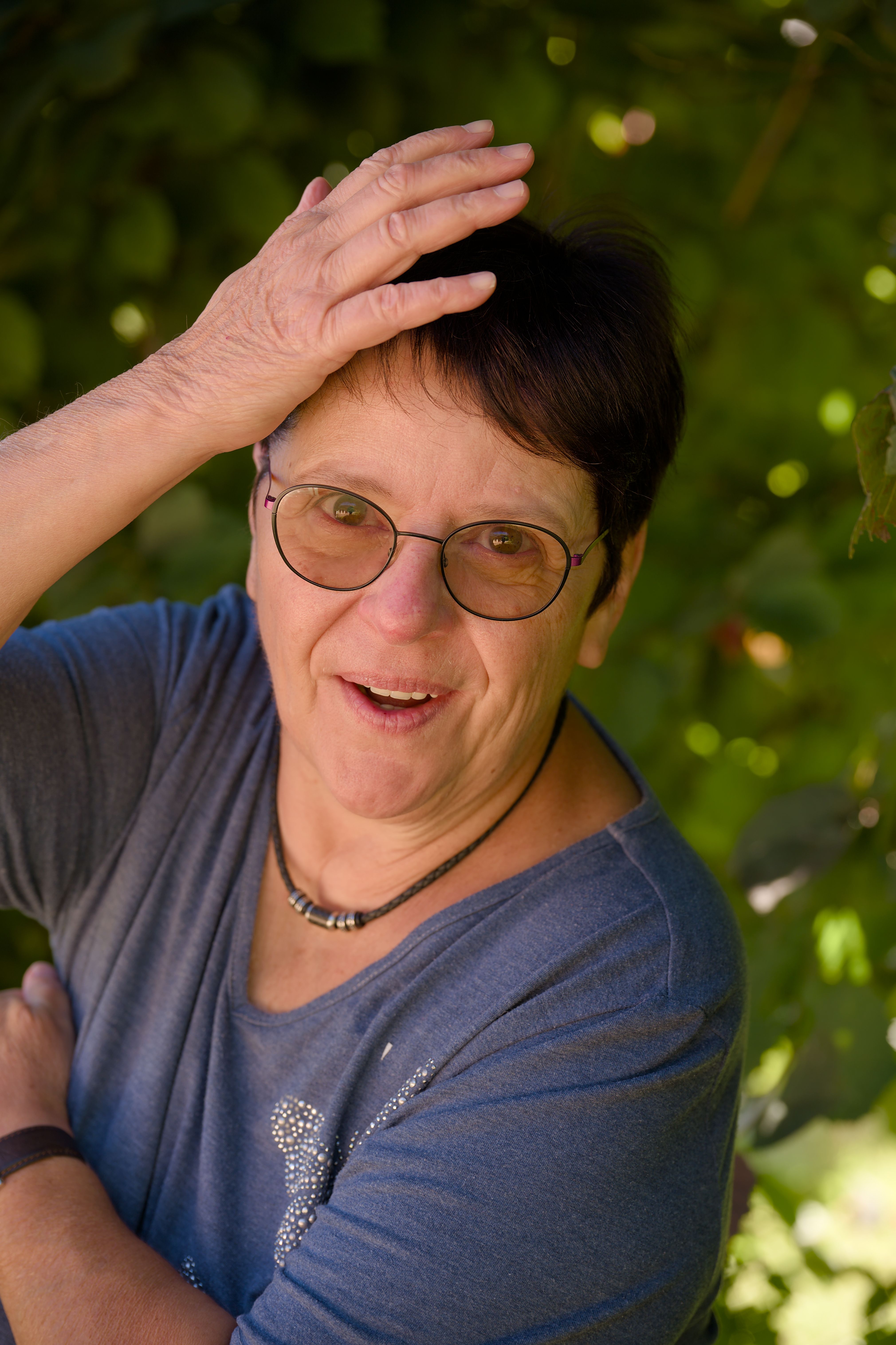 Portrait of a smiling woman outdoors with natural light and greenery.